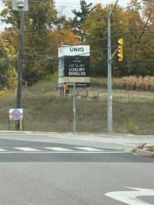 UNIQ Communities roadside sign for Mapleside Meadows advertising 40 foot and 60 foot luxury singles with a presentation gallery at 9829 Highway 27
